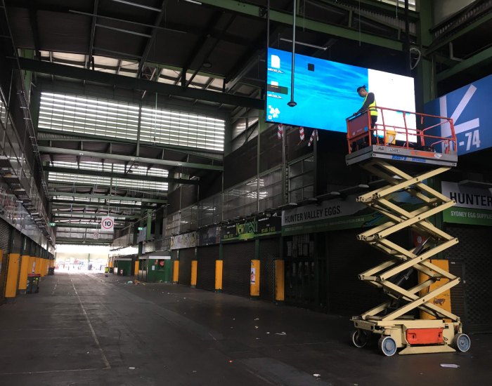 Setting up a hanging LED display from a scissor lift at Sydney Markets